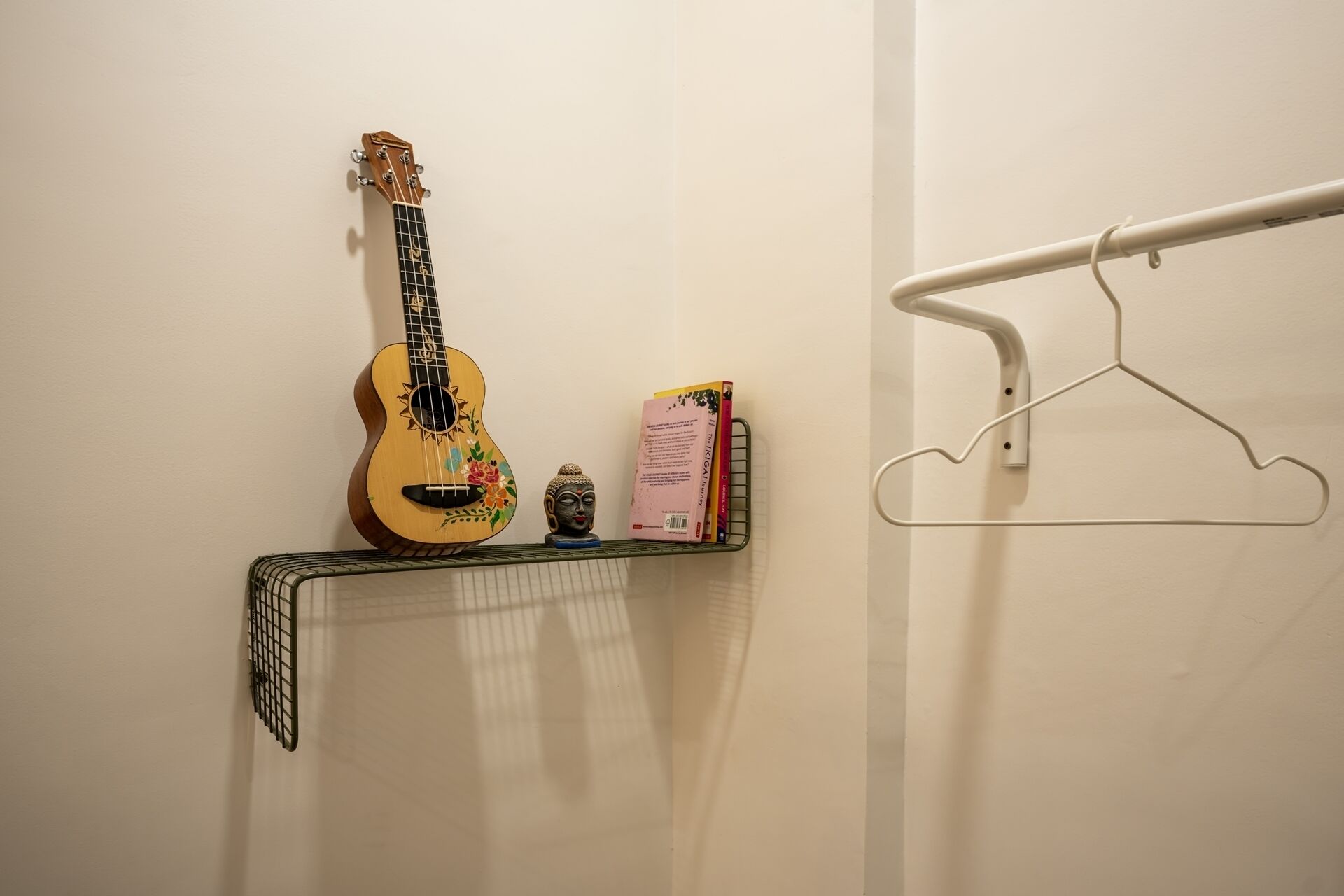 Une étagère fixée au mur, sur laquelle on peut voir un ukulélé, un livre et une statue de Bouddha.