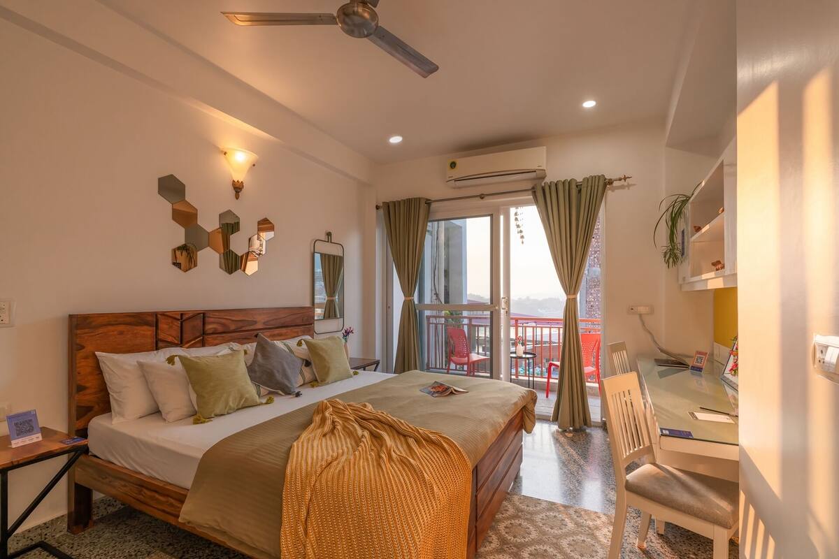Ein Hotelzimmer mit Bett, Schreibtisch, Stuhl, Deckenventilator und einem Balkon mit Blick.
