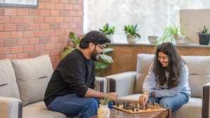 Two people playing chess on a couch in a room with a brick wall and potted plants. - LiveAway Rishikesh Laxman Jhula by PACK (Rishikesh)