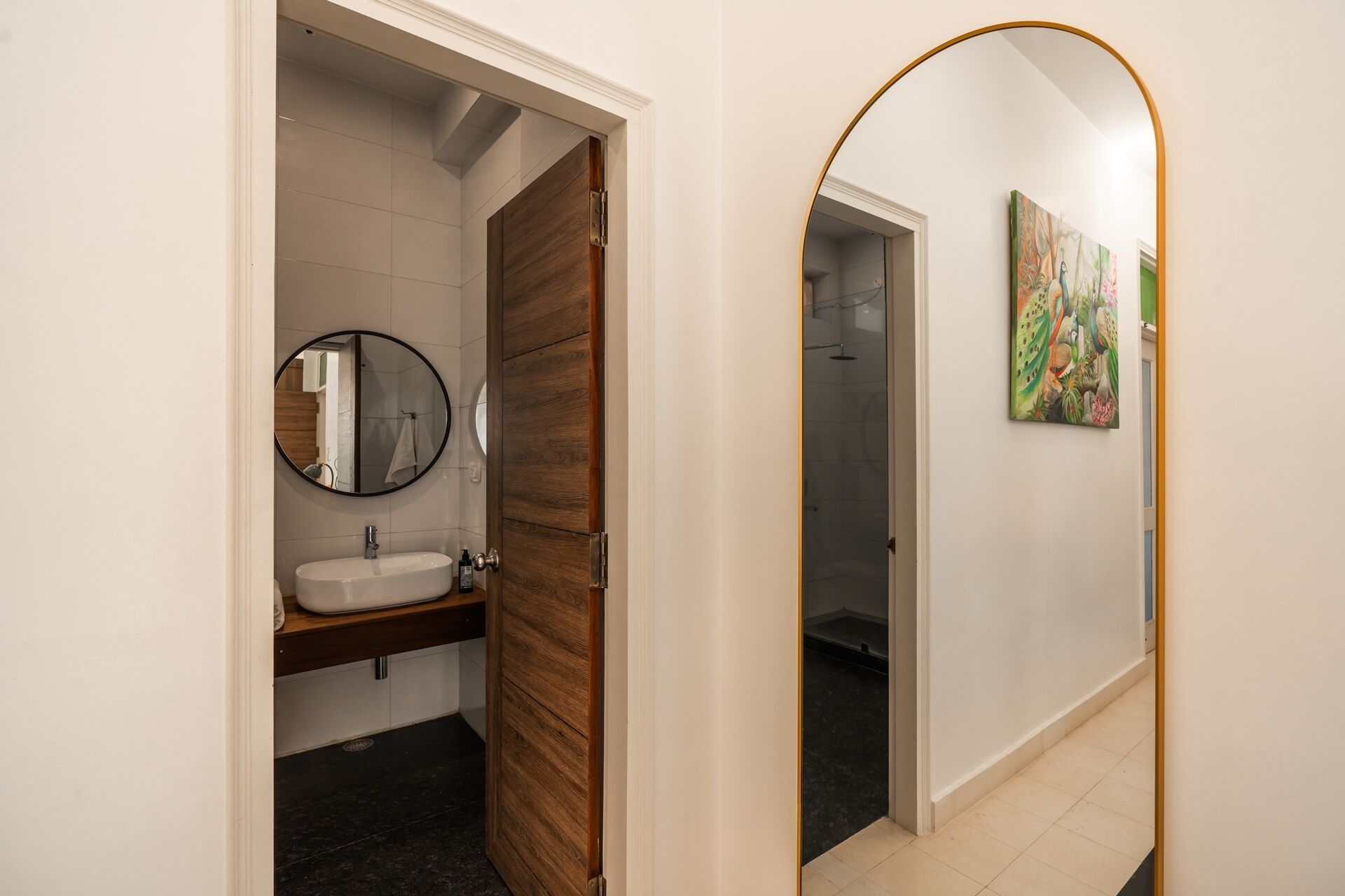 Un baño con puerta de madera, un espejo redondo y un lavamanos.