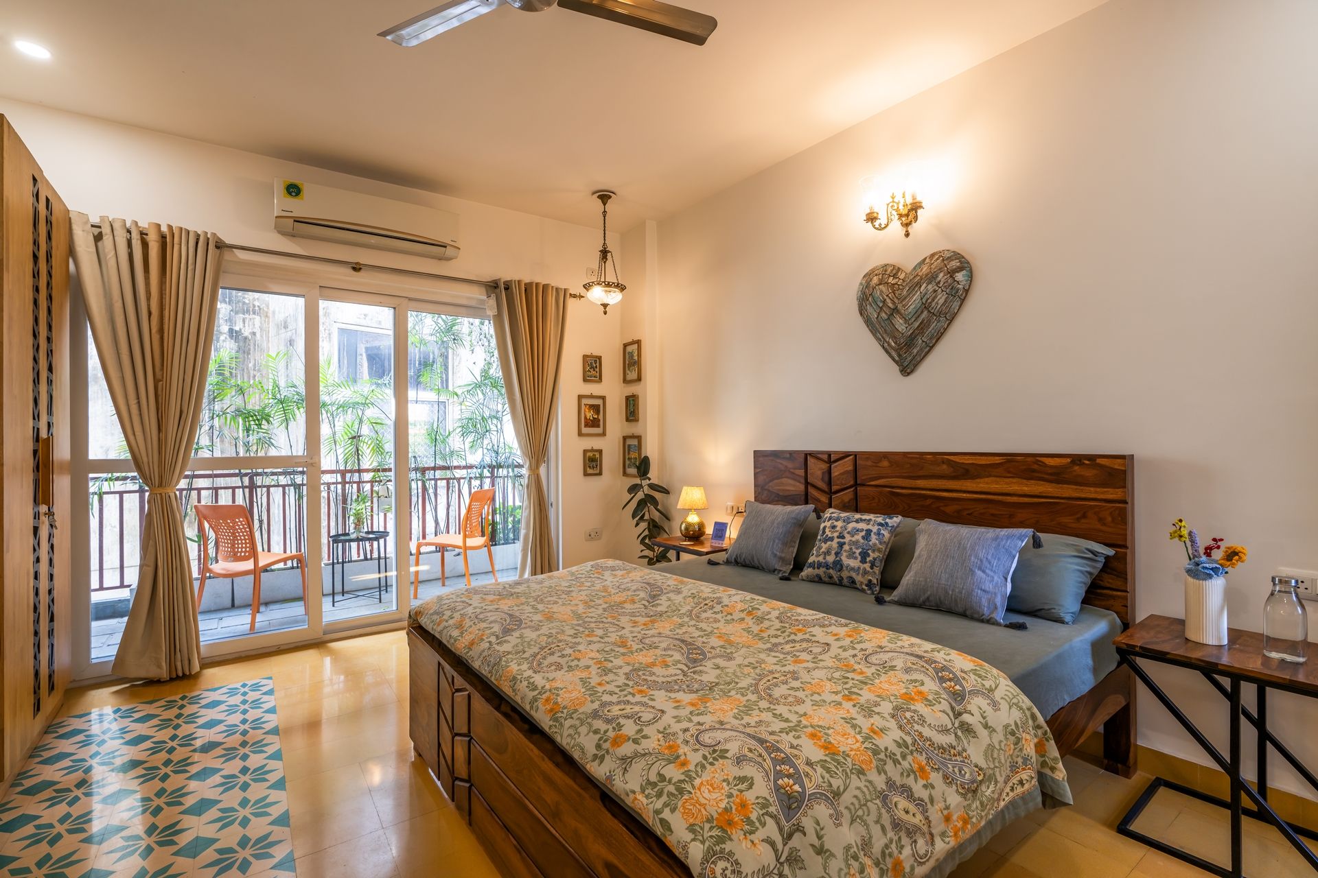A bedroom with a large bed, a balcony with chairs, and a view of greenery outside.