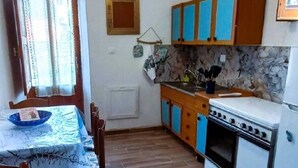 A compact kitchen with a dining table, wooden cabinets, a stove, and a window with curtains. - Grandma Maria's House - The whole house for you (Scilla)