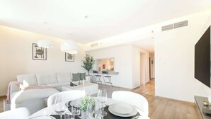 Un soggiorno moderno con zona pranzo apparecchiata per un pasto. Si vedono un divano, un tavolino e un tavolo da pranzo con sedie. Una televisione è montata a destra sulla parete.