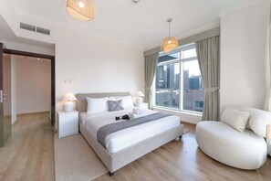 A modern hotel room with a large bed, bedside lamps, a sofa, and a view of the city through large windows. - Free housekeeping visits during your stay - StayShort - Stylish 2BR Apartment in Downtown Sleeps 4 (Downtown)