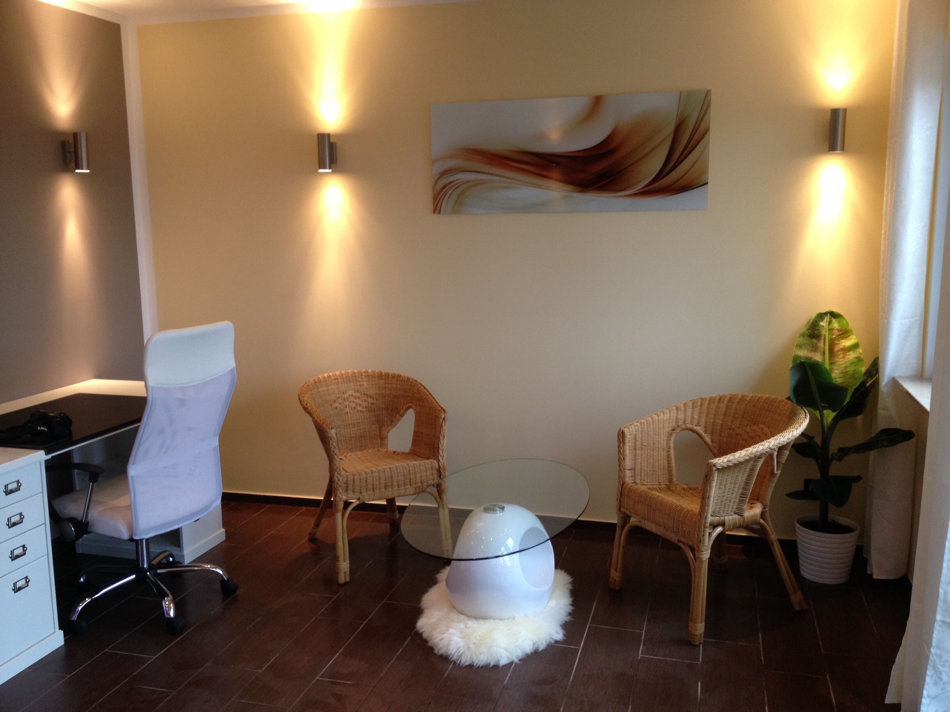 A modern waiting area with wicker chairs, a glass table, and a white chair with a white cushion.