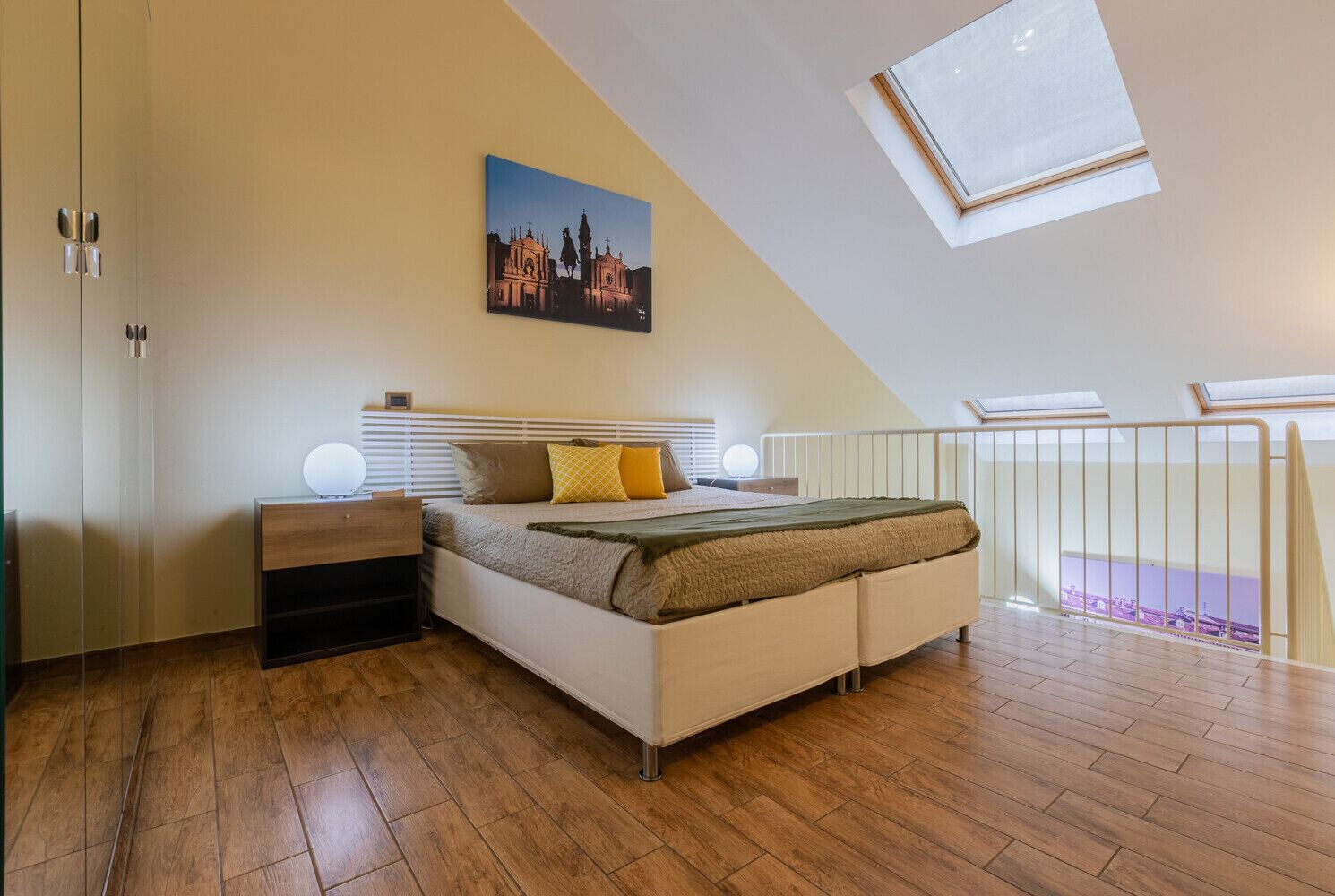 A bedroom with a bed, bedside tables, a nightstand, a painting, and a skylight.
