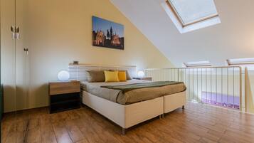 A bedroom with a bed, bedside tables, a nightstand, a painting, and a skylight.