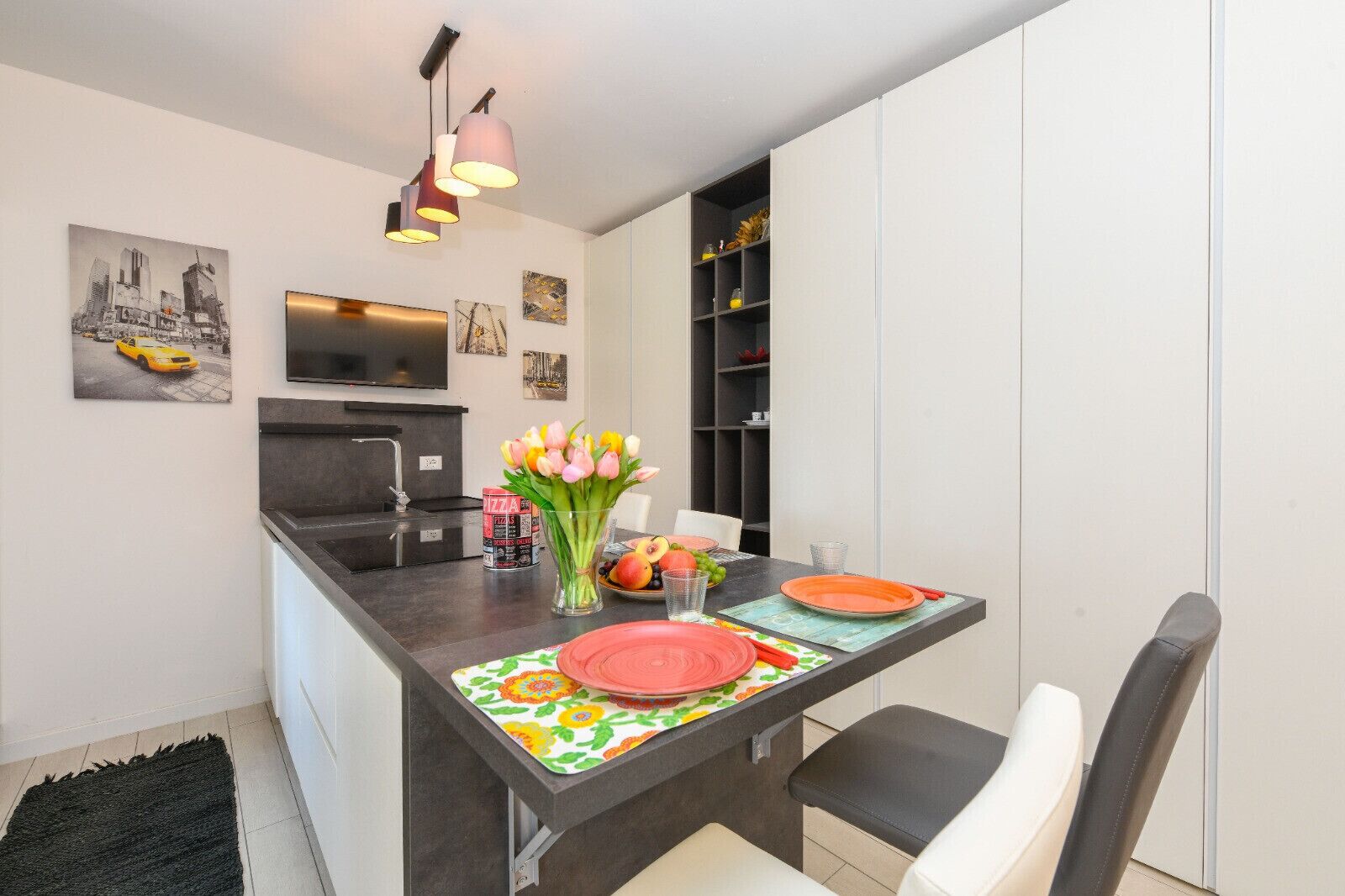A modern kitchen with a dining area, featuring a black countertop, white cabinets, and a black rug.