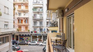 A balcony with a table and chairs, overlooking a street with parked cars and a bookstore. - Eleanor by halu! - 1-BD Apartment next to Hagia Sophia (Thessaloniki)