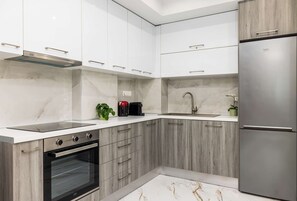 Una cocina moderna con armarios blancos, horno empotrado, refrigerador de acero inoxidable y salpicadero de mármol.