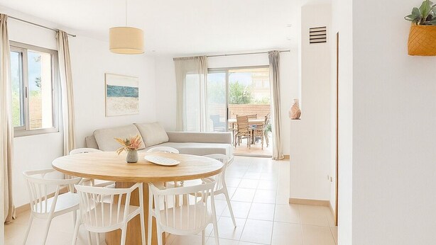 A bright, spacious dining area with a round wooden table and white chairs, a sofa, and a hanging plant.