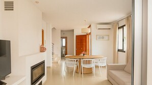 A modern living room with a flat-screen TV, fireplace, dining table with chairs, and a sofa.