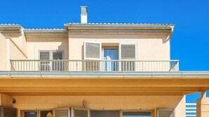A two-story house with a balcony, a patio with outdoor furniture, and a garden with white pebbles and palm trees.