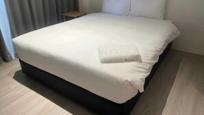 Ein ordentlich bezogenes Bett mit weißen Leinentüchern und einem gefalteten Handtuch.