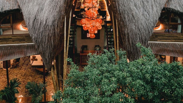 A thatched-roof structure with a central open area, surrounded by lush greenery and a mountainous backdrop.
