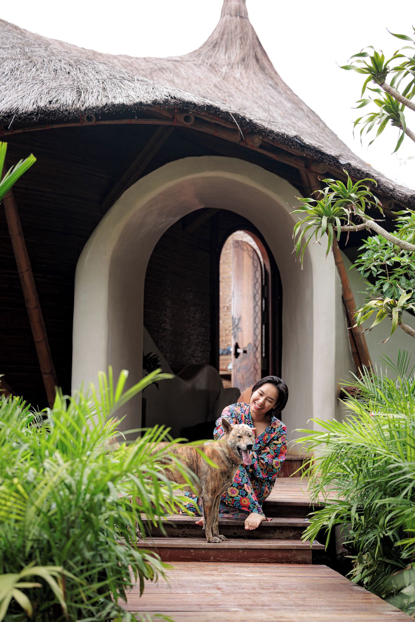 A person sitting on steps in front of a building with a thatched roof and an arched doorway.