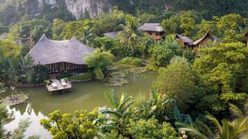 A tropical resort with thatched-roof cottages, a pond with lily pads, and lush greenery.