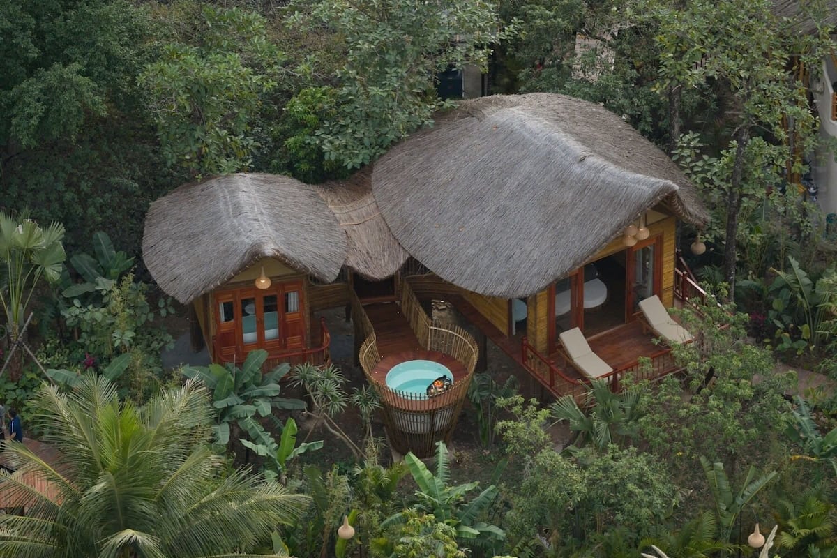 Una cabaña con techo de paja y piscina, rodeada de exuberante vegetación tropical.