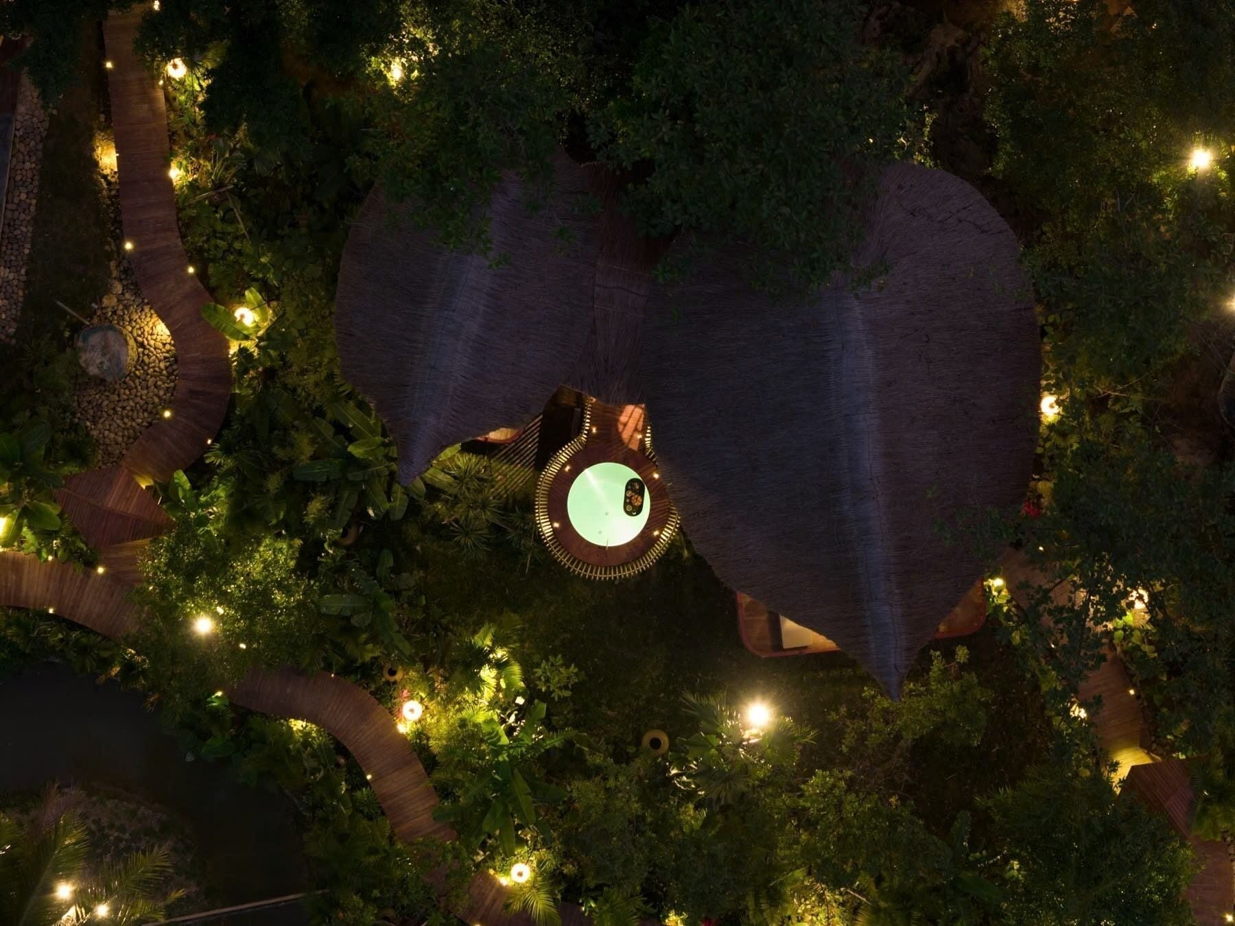 An aerial view of a lush garden with a circular structure featuring a central light fixture surrounded by foliage.
