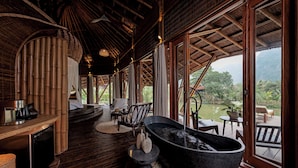 A spa area with a large stone bathtub, wooden flooring, and a view of a lake and mountains.