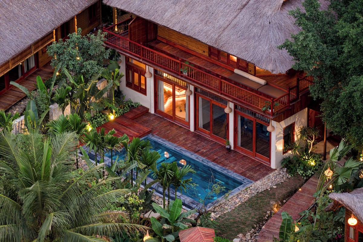 Un resort con piscina, edificios de techo de paja y abundante follaje.
