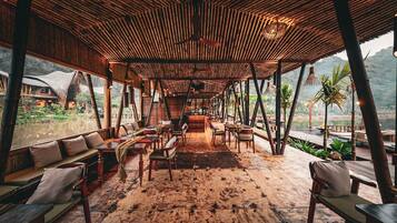 An open-air dining area with wooden furniture and a thatched roof.