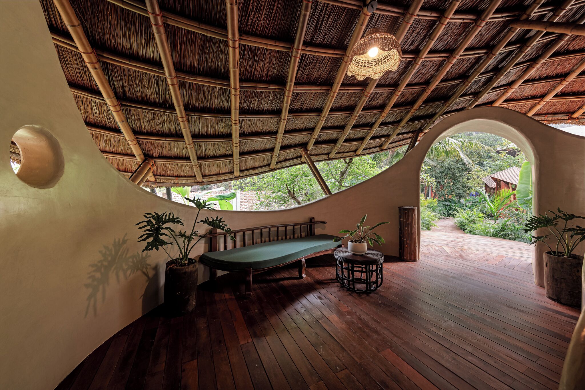 A room with a curved wooden floor, a green bench, and a bamboo ceiling.