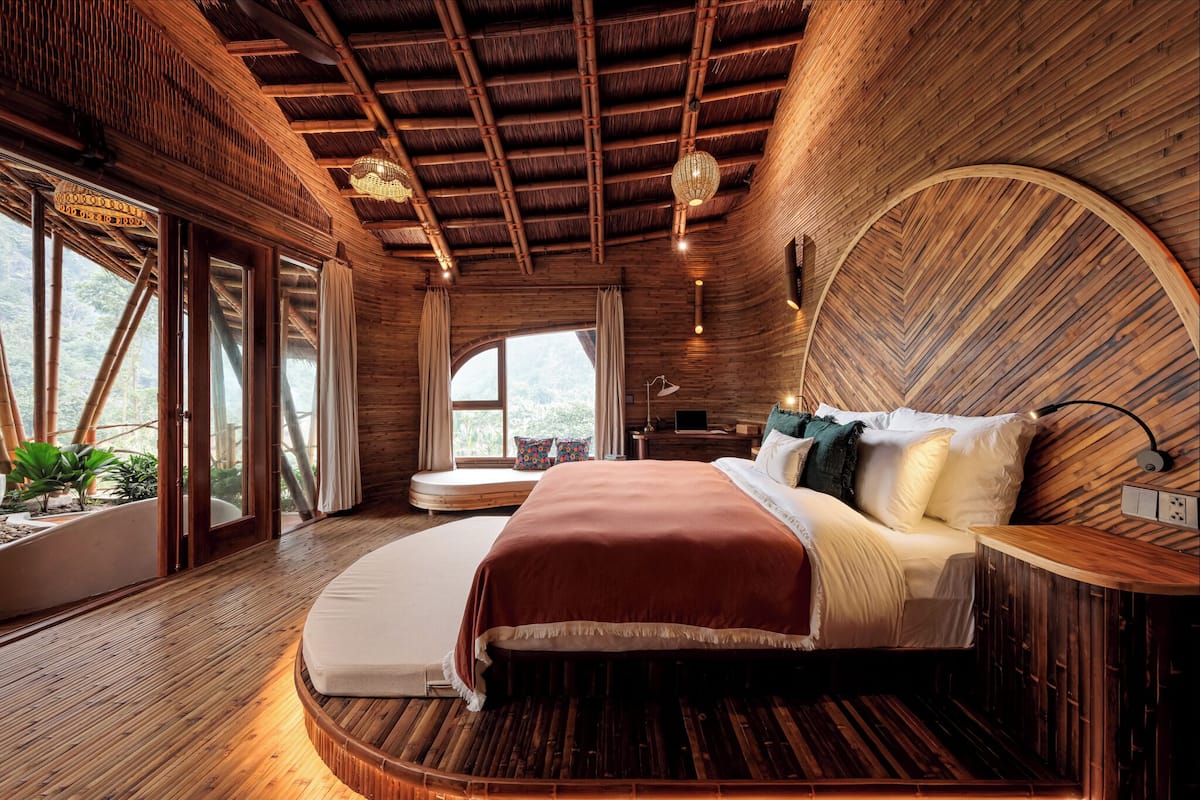 Dormitorio con decoración de madera, una cama grande, una pared curva y ventana con vistas a la vegetación.