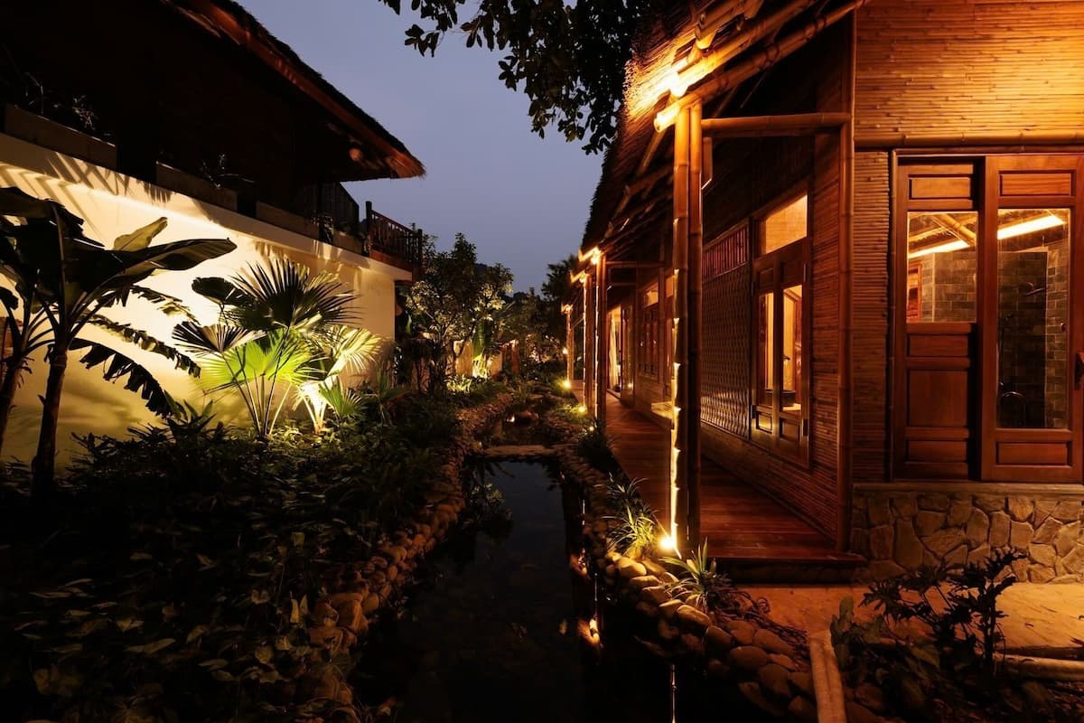 Un edificio tradicional de madera con techo de paja, un estrecho canal de agua e iluminación exterior.