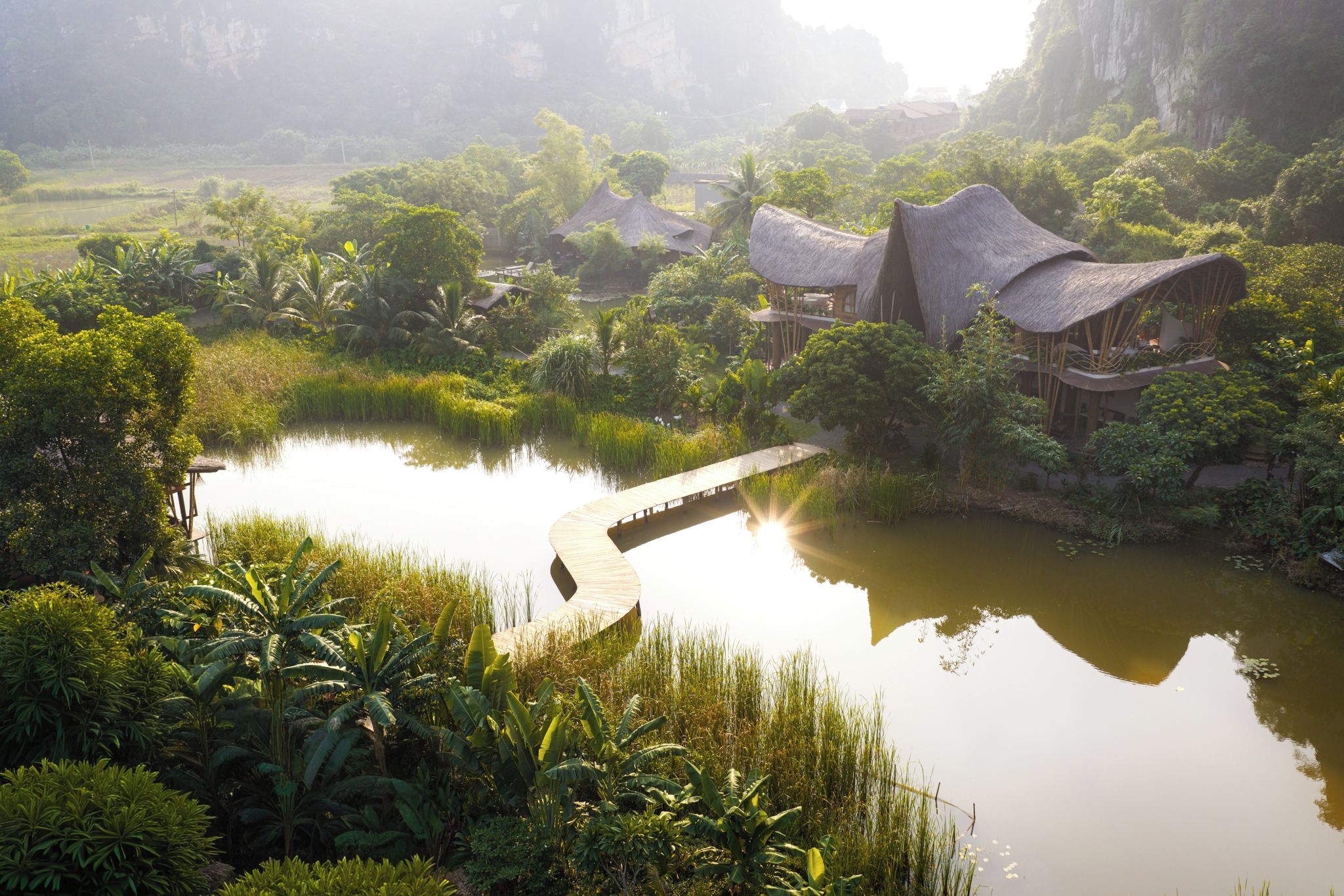 A serene riverside setting with thatched-roof structures and lush greenery.