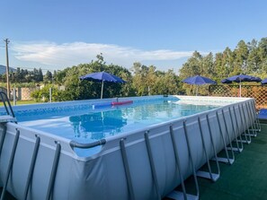 A rectangular above-ground pool with a ladder on one side, surrounded by a fence and blue umbrellas. - Casa Gli Allori - Iglesias (Iglesias)
