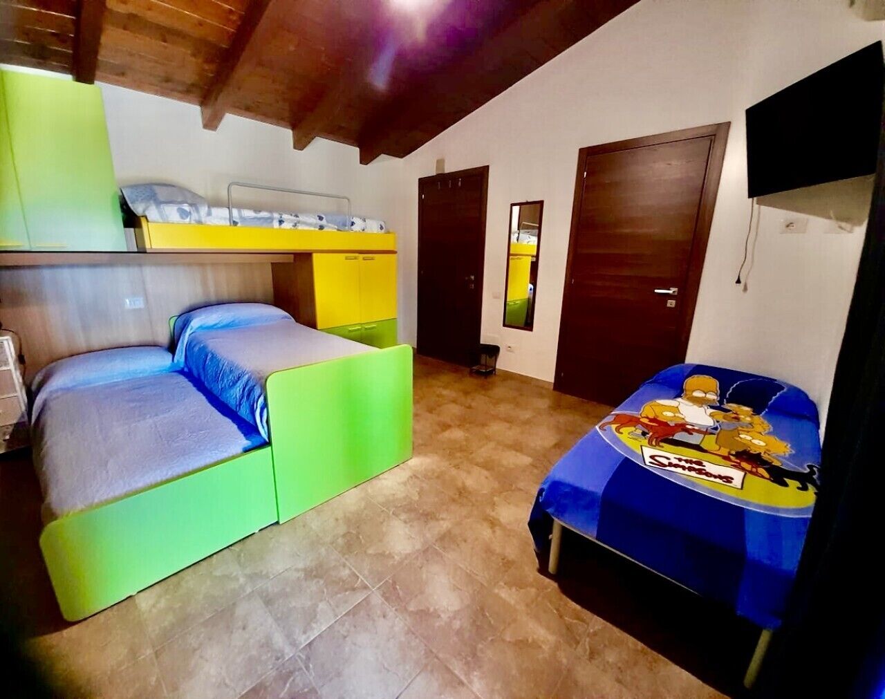 A room with bunk beds, a small table with a Simpsons-themed tablecloth, and a TV mounted on the wall.