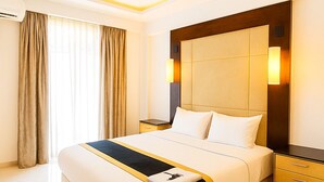 A hotel room with a large bed, a ceiling fan, a nightstand, and a wall-mounted lamp. - Luxury 1401 Pixiestays With Free Parking (Mumbai)