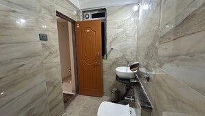 A bathroom with a marble wall, a toilet, a sink with a mirror, and a shower area. - Luxury 1401 Pixiestays With Free Parking (Mumbai)