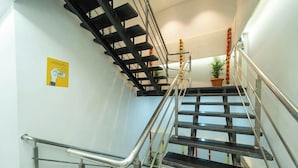 Una escalera con barandillas metálicas y pasamanos, que lleva a un rellano con una planta en maceta.