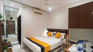 Una habitación de hotel moderna con cama, mesita de noche y escritorio con silla. Se observa un equipo de aire acondicionado en la pared y un ventilador de techo.
