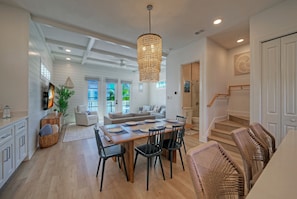 A spacious living area with a dining table, chairs, and a chandelier. There is a staircase leading to another level, and a sofa in the background. - Pool + Boardwalk Access + Steps from the Beach | Villa Blanca by AvantStay (Port Aransas)