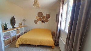 Une chambre avec un lit jaune, une étagère ornée d’objets décoratifs, un mur décoré de paniers tressés et une fenêtre avec des rideaux.