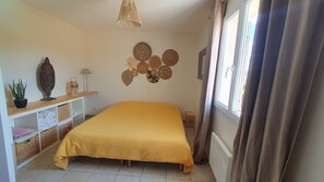 Ein Schlafzimmer mit einem gelben Bett, einem Regal mit Dekorationen, einer Wand mit gewebten Körben und einem Fenster mit Vorhängen.