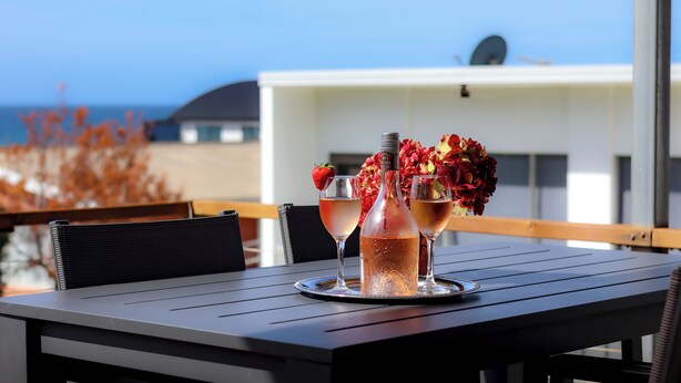 A table with two glasses of a pink drink, a bottle, and a bouquet of flowers on a tray. - Short walk to the beach and local cafes (Penguin)