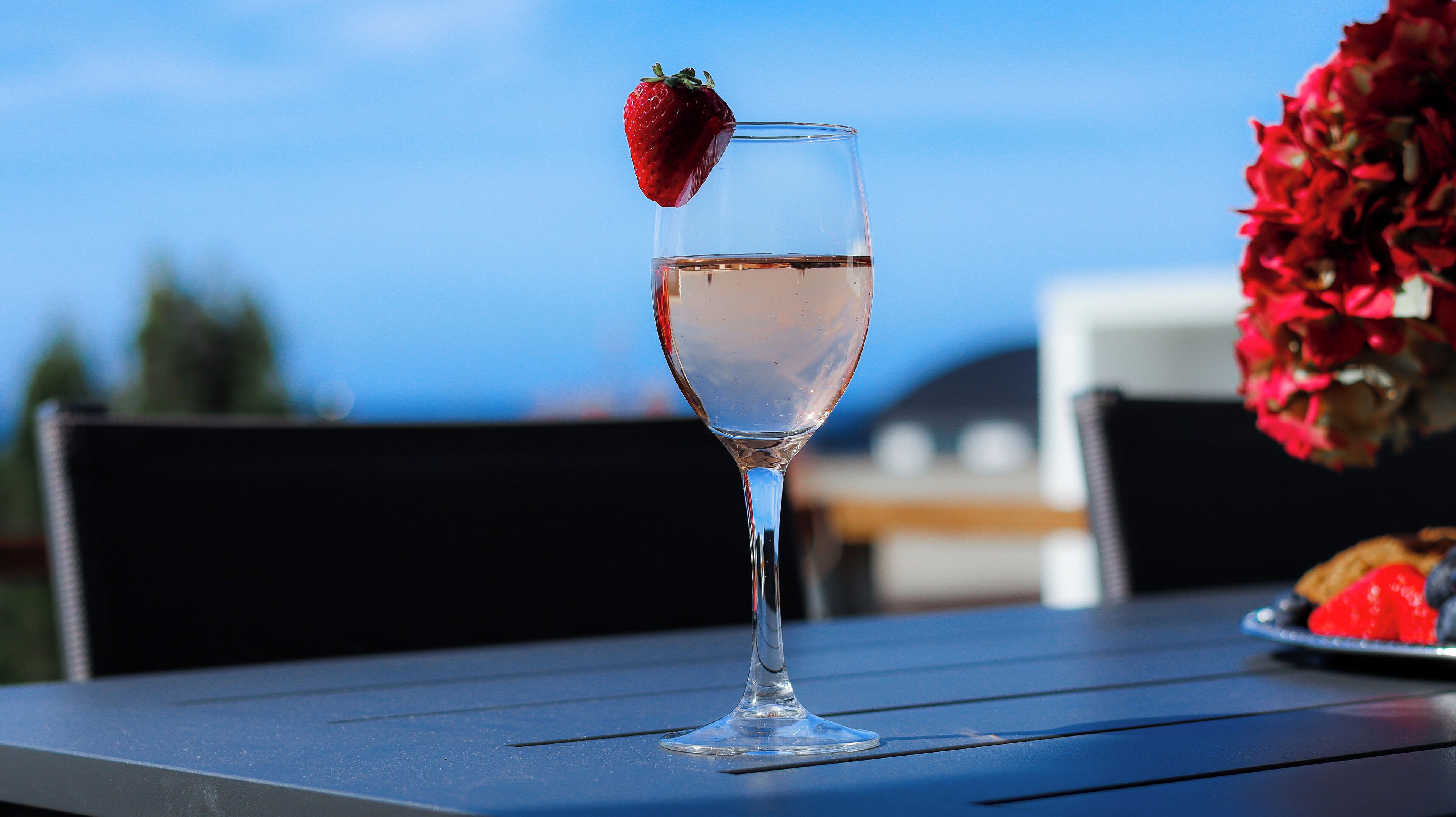 A glass of clear liquid with a strawberry garnish on a table outdoors.