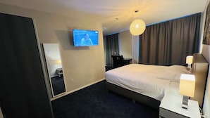 Une chambre d’hôtel avec un grand lit, une table de chevet avec une lampe, un téléviseur fixé au mur et un lustre moderne.