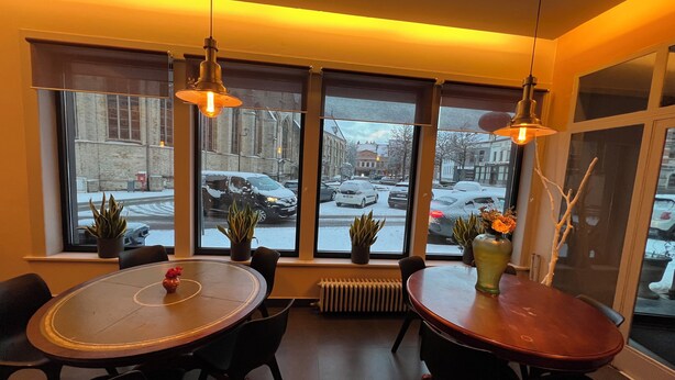Un coin repas avec une table ronde et des chaises, des plantes en pot et de grandes fenêtres donnant sur une rue enneigée.