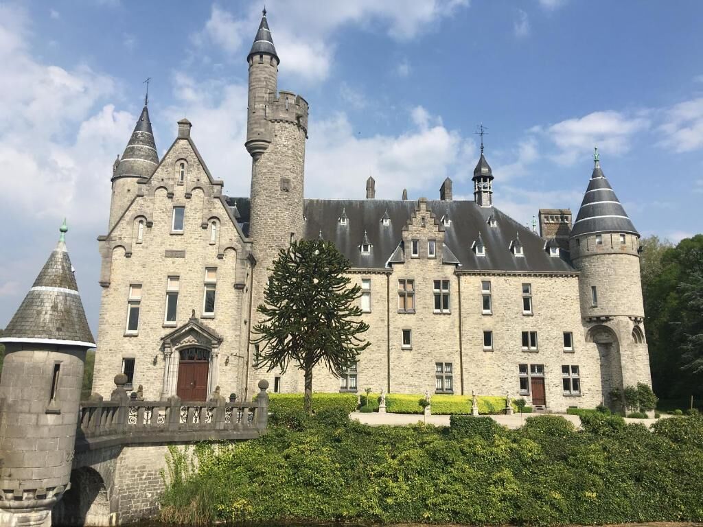 A historic stone castle with multiple towers, a central courtyard, and well-maintained hedges.