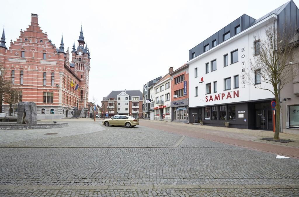 A cobblestone street with a historic building and a modern hotel named "SAMPAN" on the right.