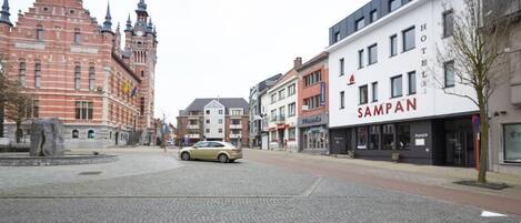 A cobblestone street with a historic building and a modern hotel named "SAMPAN" on the right.