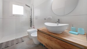 Un baño moderno con un lavamanos ovalado grande, un mueble de tocador de madera, un inodoro y una zona de ducha.