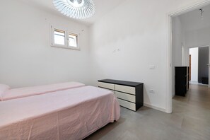 Een slaapkamer met twee bedden, een dressoir, een raam en een deur naar een andere kamer.