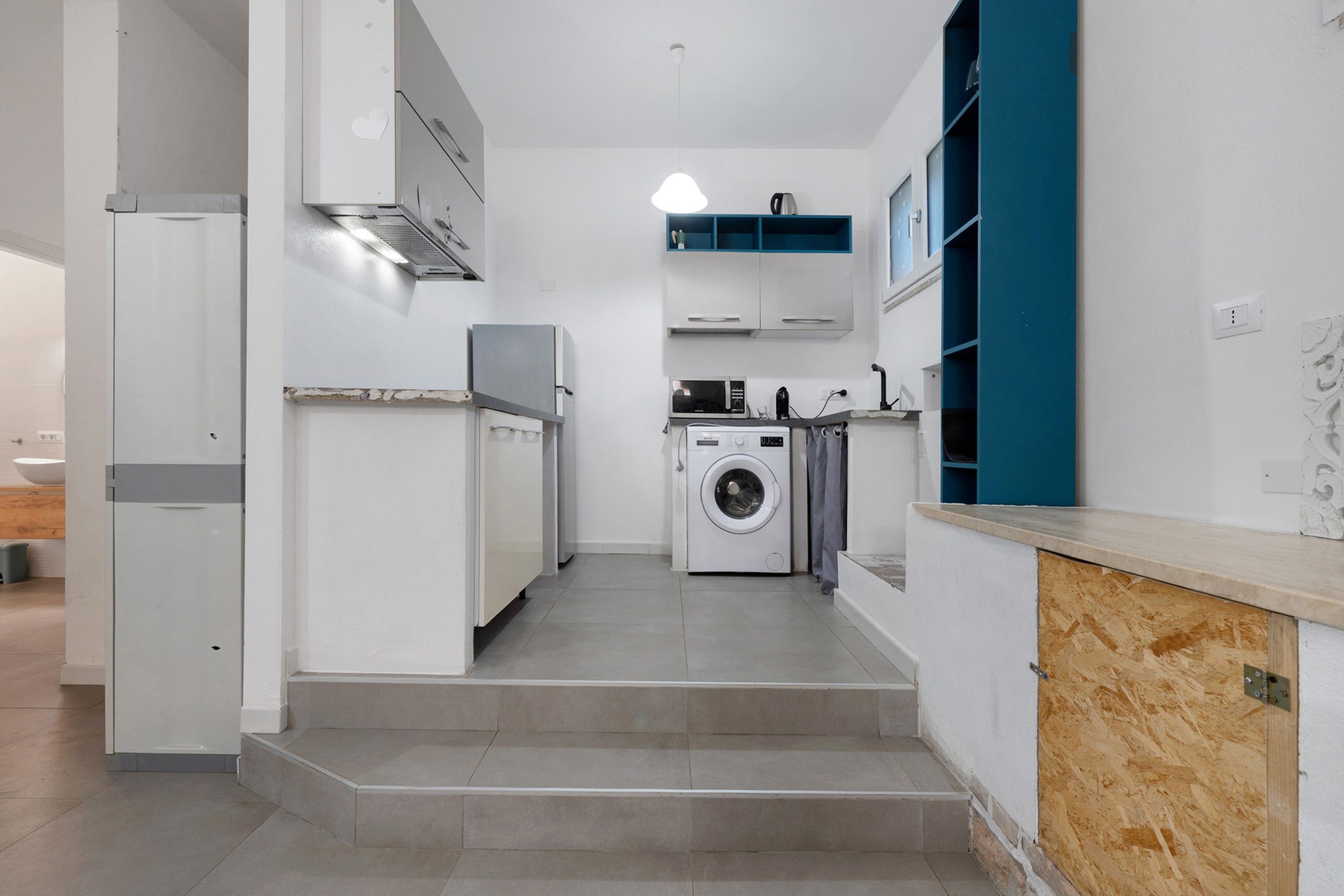 Een kleine keuken met een wasmachine, een magnetron en een inbouwoven.