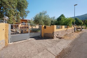 A gated entrance with a metal gate, a stone wall, and a street lamp. - Thilimba Holiday Home: Your Oasis of Tranquility in Southern Sardinia (Poggio Dei Pini)